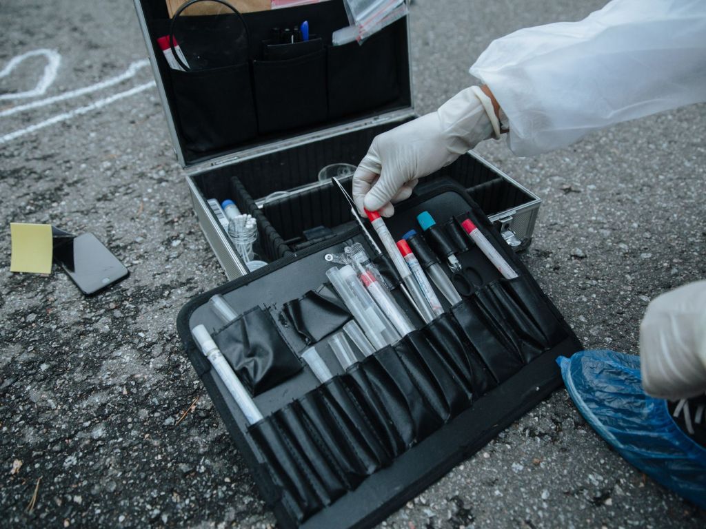 Perito con guantes junto a un maletín de recolección de evidencia en un sitio del suceso