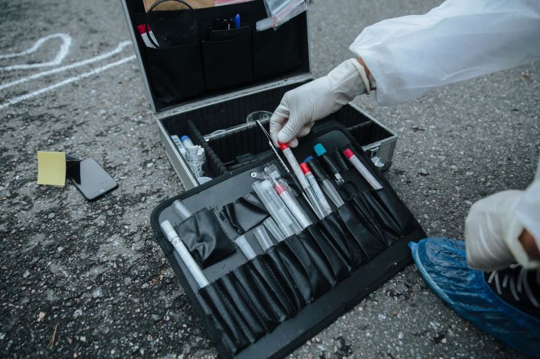 Perito con guantes junto a un maletín de recolección de evidencia en un sitio del suceso